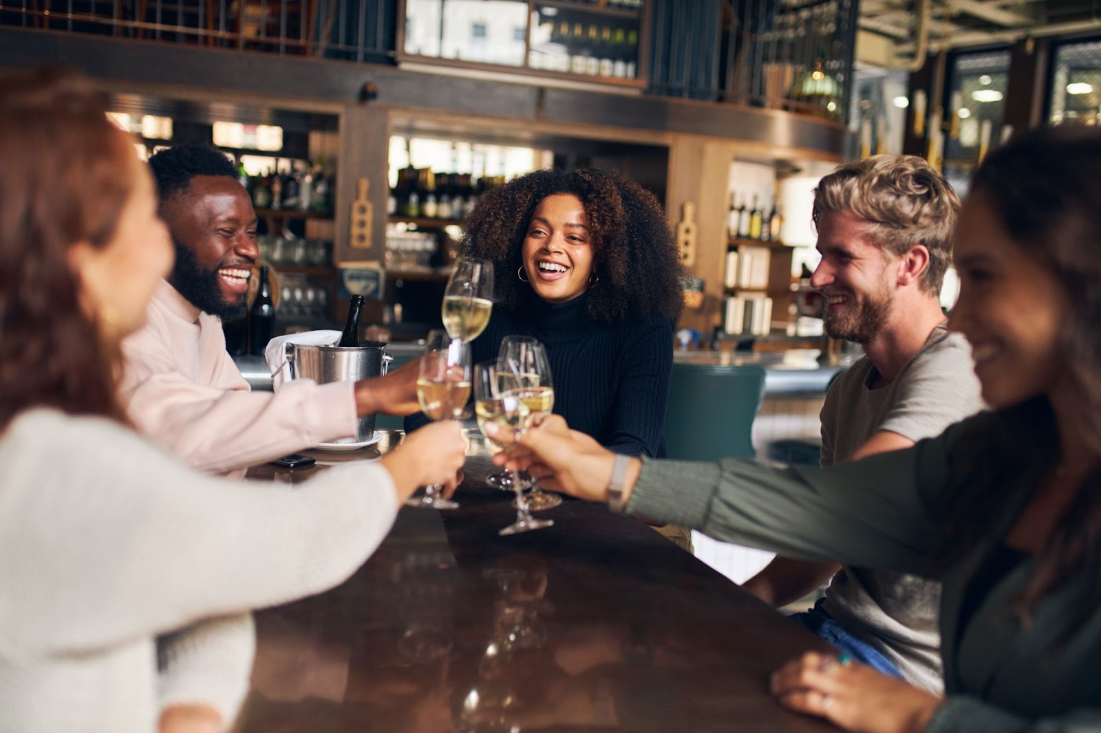 A group of friends joyfully toasting with glasses at a wine bar celebrating their time together over food and winejpeg
