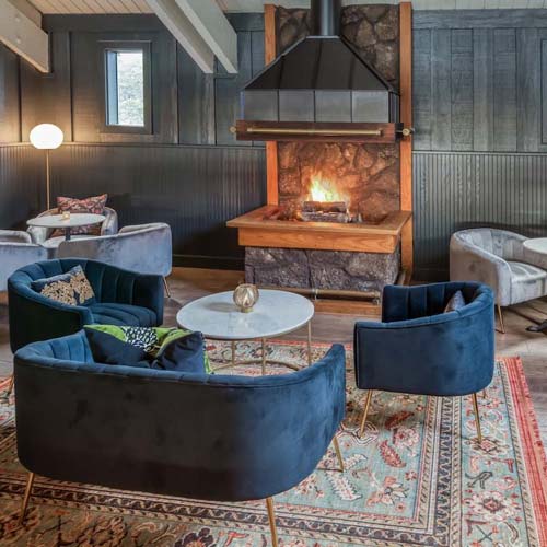 A seating area with elegant blue velvet chairs, circled around a marble coffee table, next to a warm fireplace